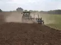 Traktor z pługiem wykonuje uprawę bezorkową, wzbijając tumany kurzu na polu.