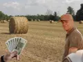Rolnik z uśmiechem na twarzy, w tle pole ze słomianymi balotami. W ręce trzyma banknoty, zastanawiając się, ile waży balot słomy.
