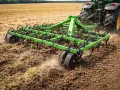 Zielony kultywator z zębami spulchnia ziemię na polu, przygotowując ją do siewu. To jest właśnie kultywator.