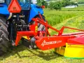 Kosiarka rotacyjna Mesko-Rol Z 175-1 zamontowana z tyłu niebieskiego traktora, gotowa do pracy na zielonej łące.