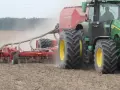 Zielony traktor z przyczepioną maszyną wykonuje wałowanie pola, podnosząc tumany kurzu.