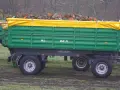Zielona przyczepa Fortschritt HL 80.11 z drewnem pod żółtą plandeką.