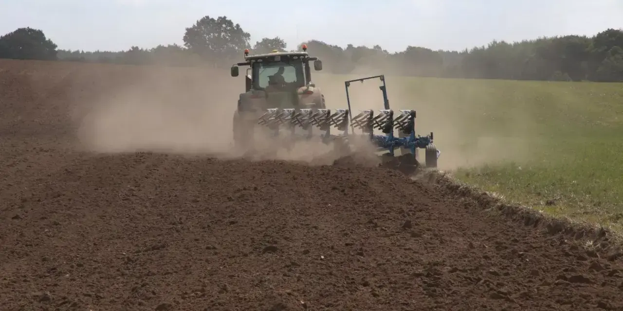 Traktor z pługiem wykonuje uprawę bezorkową, wzbijając tumany kurzu na polu.