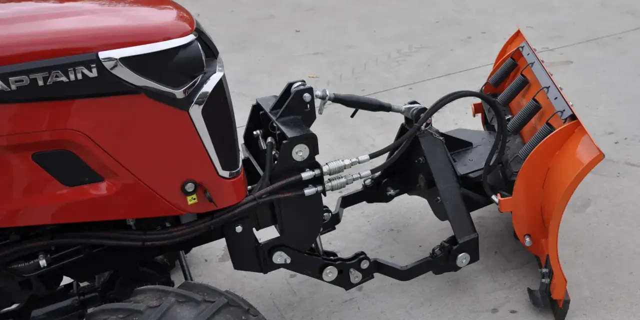 Czerwony traktor z zamontowanym z przodu pługiem śnieżnym. To jest **tuz** do pługa.