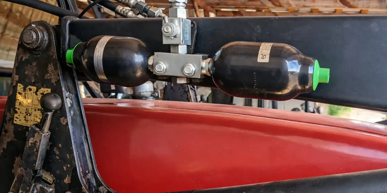 Dwa akumulatory hydrauliczne zamontowane na ładowaczu. Pomocne przy wyborze, jak dobrać akumulator hydrauliczny do maszyn rolniczych.