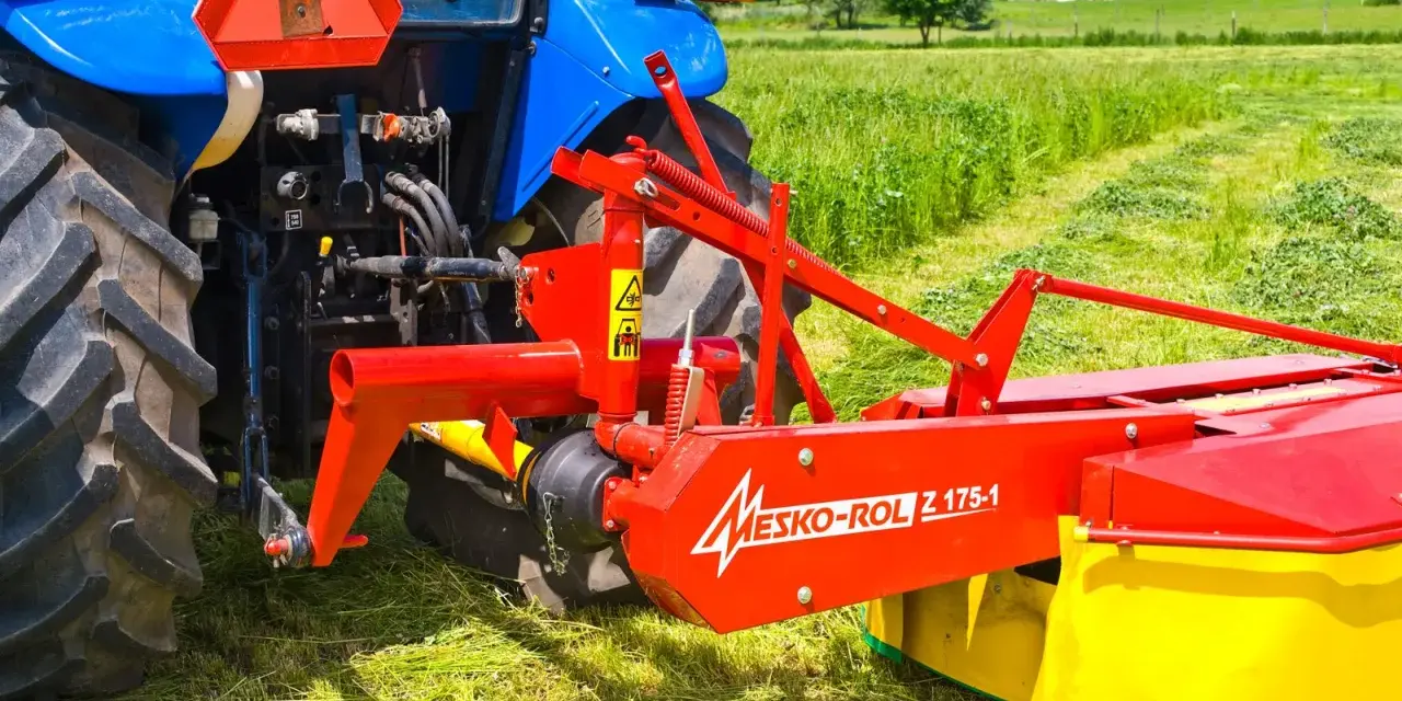 Kosiarka rotacyjna Mesko-Rol Z 175-1 zamontowana z tyłu niebieskiego traktora, gotowa do pracy na zielonej łące.