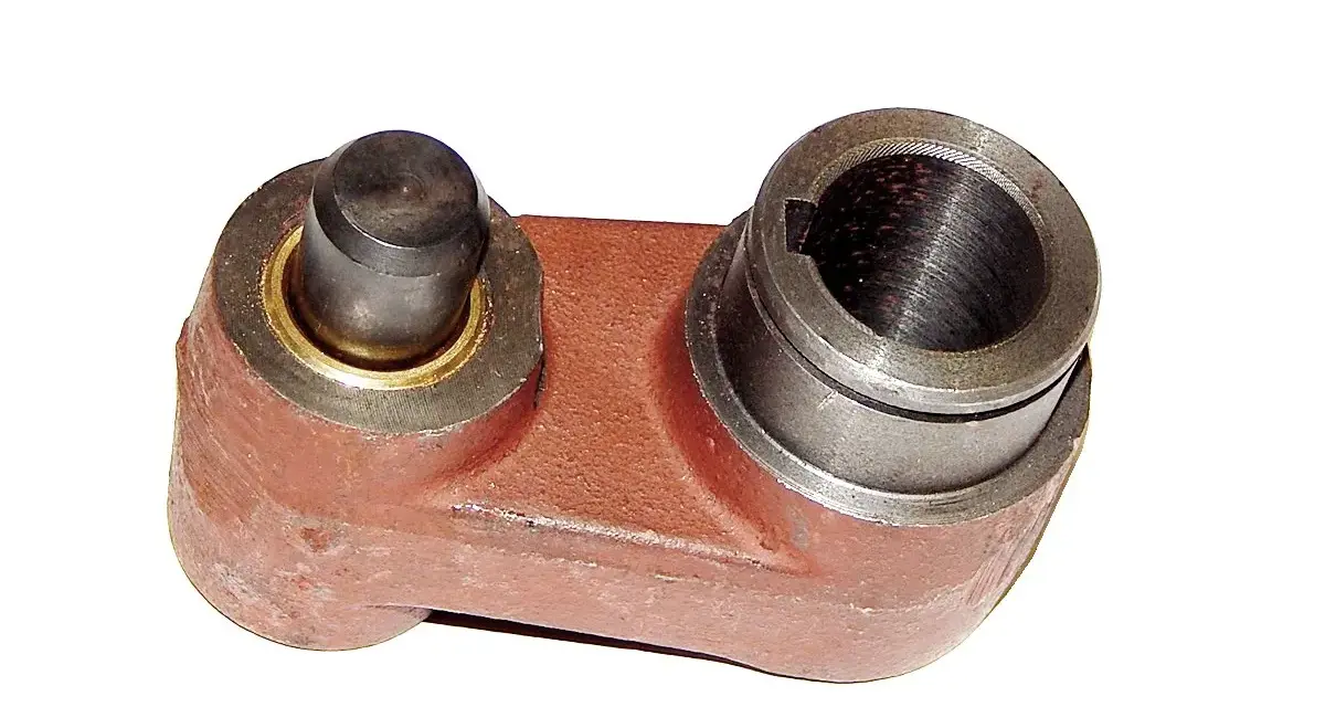 Metalowy element, prawdopodobnie sprzęgło kosiarki rotacyjnej, z jednym bolcem i jednym gniazdem na wałek.