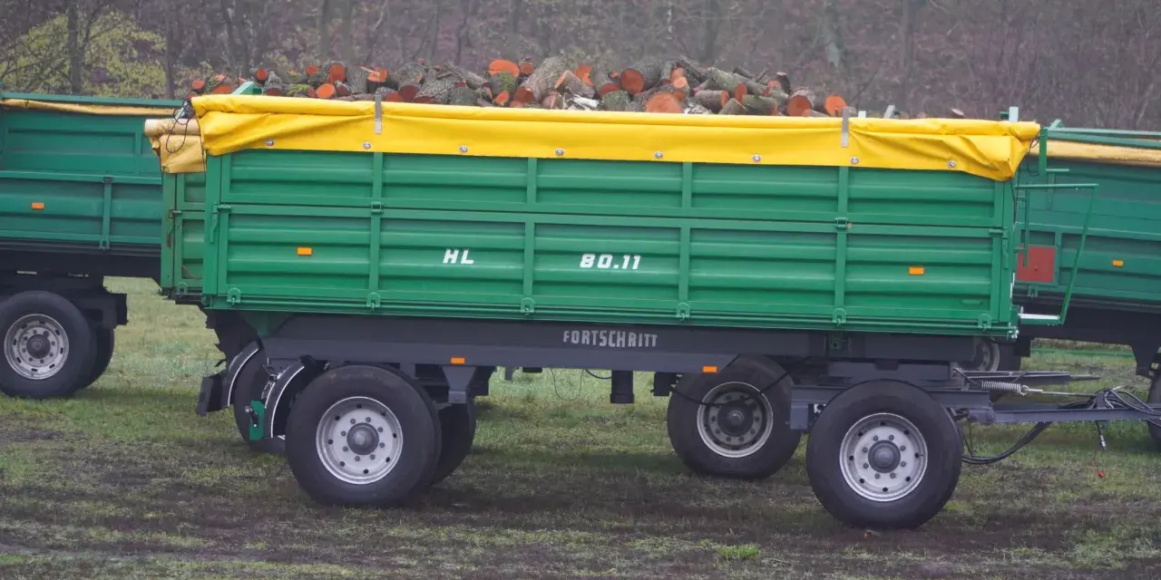 Zielona przyczepa Fortschritt HL 80.11 z drewnem pod żółtą plandeką.