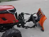 Czerwony traktor z zamontowanym z przodu pługiem śnieżnym. To jest **tuz** do pługa.