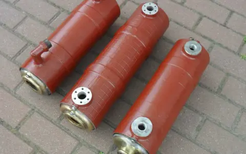 Trzy cylindryczne elementy, prawdopodobnie części maszyny rolniczej, jak filtr oleju bizon. Mają brązowy kolor i metalowe zakończenia.