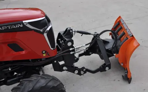 Czerwony traktor z zamontowanym z przodu pługiem śnieżnym. To jest **tuz** do pługa.