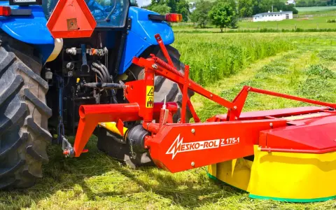 Kosiarka rotacyjna Mesko-Rol Z 175-1 zamontowana z tyłu niebieskiego traktora, gotowa do pracy na zielonej łące.