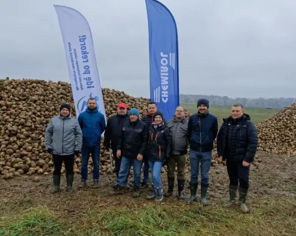 Grupa rolników pozuje na tle ogromnych hałd buraków cukrowych. Wynik tegorocznych zbiorów, pokazujący ile ton buraka cukrowego z hektara, robi wrażenie.