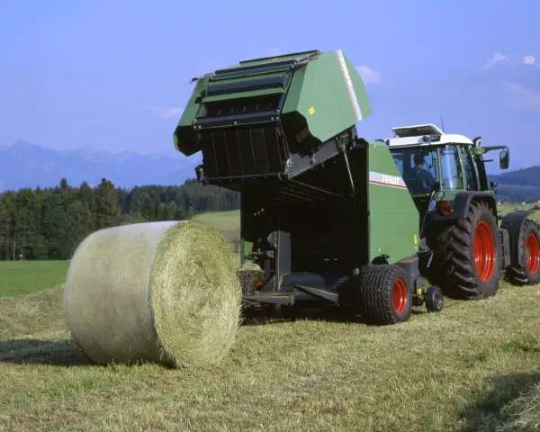 Zielone prasy rolujące małe zapotrzebowanie mocy pracują na polu, tworząc bele siana.