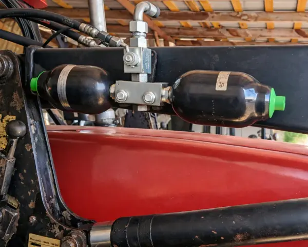Dwa akumulatory hydrauliczne zamontowane na ładowaczu. Pomocne przy wyborze, jak dobrać akumulator hydrauliczny do maszyn rolniczych.