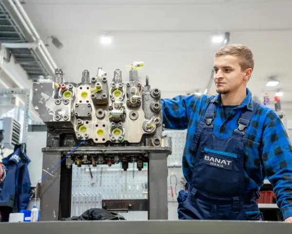 Mechanik w niebieskim kombinezonie pracuje nad budową rozdzielacza hydraulicznego w warsztacie.