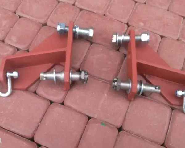 Części do t25 jak zamontować cięgno boczne podnośnika. Metalowe elementy z śrubami i nakrętkami na czerwonej kostce.