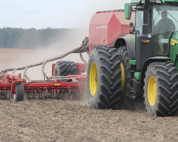 Zielony traktor z przyczepioną maszyną wykonuje wałowanie pola, podnosząc tumany kurzu.