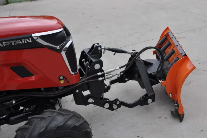 Czerwony traktor z zamontowanym z przodu pługiem śnieżnym. To jest **tuz** do pługa.