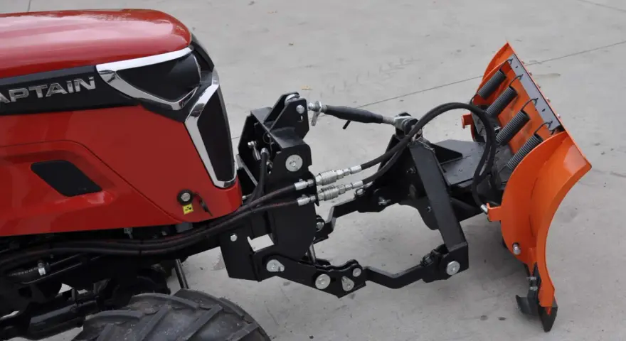 Czerwony traktor z zamontowanym z przodu pługiem śnieżnym. To jest **tuz** do pługa.