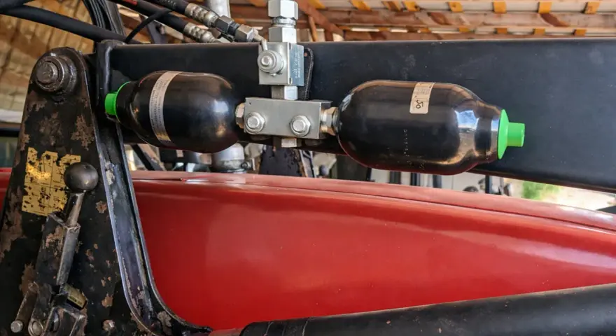 Dwa akumulatory hydrauliczne zamontowane na ładowaczu. Pomocne przy wyborze, jak dobrać akumulator hydrauliczny do maszyn rolniczych.
