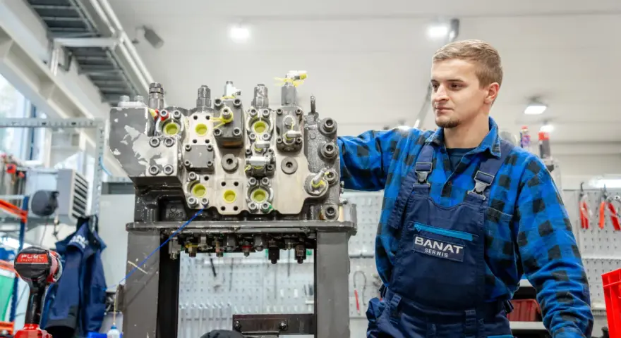 Mechanik w niebieskim kombinezonie pracuje nad budową rozdzielacza hydraulicznego w warsztacie.
