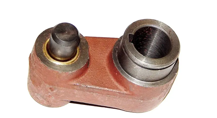 Metalowy element, prawdopodobnie sprzęgło kosiarki rotacyjnej, z jednym bolcem i jednym gniazdem na wałek.