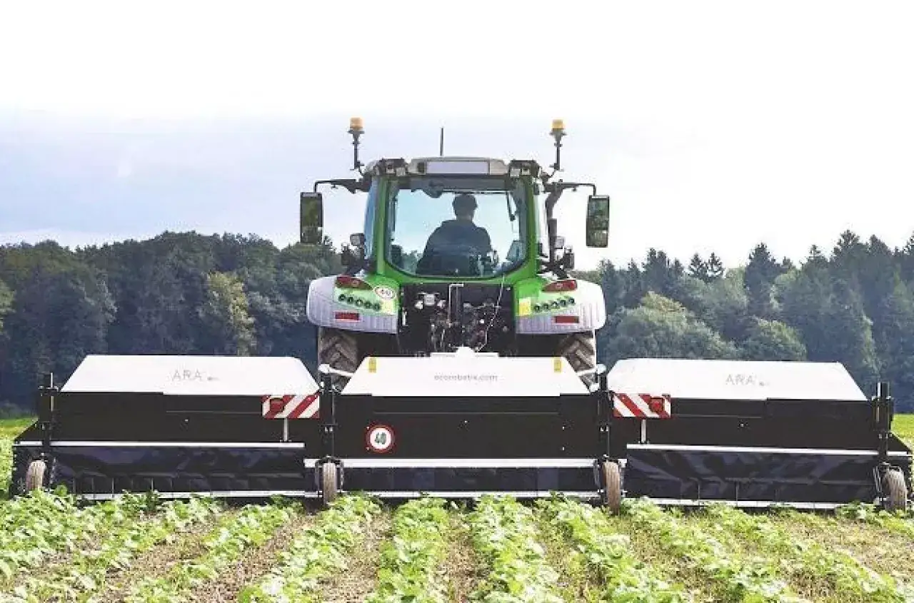 Zielony traktor z szerokim opryskiwaczem na zielsko pracuje na polu.