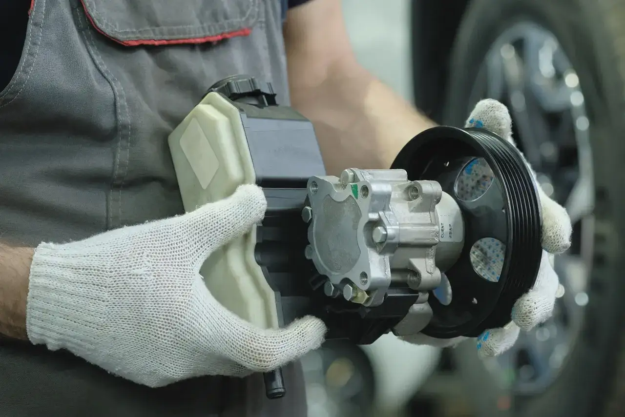Mechanik w białych rękawiczkach trzyma pompę hydrauliczną i zbiorniczek płynu. Jak sprawdzić czy pompa hydrauliczna jest dobra?