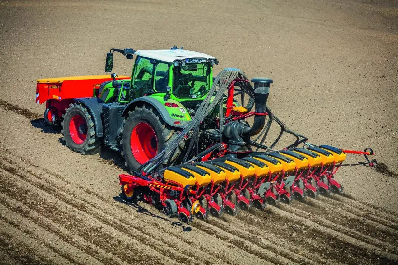 Zielony traktor z siewnikiem precyzyjnym wykonuje wysiew soi na 1 ha. Maszyna równomiernie rozsiewa nasiona w przygotowane bruzdy.