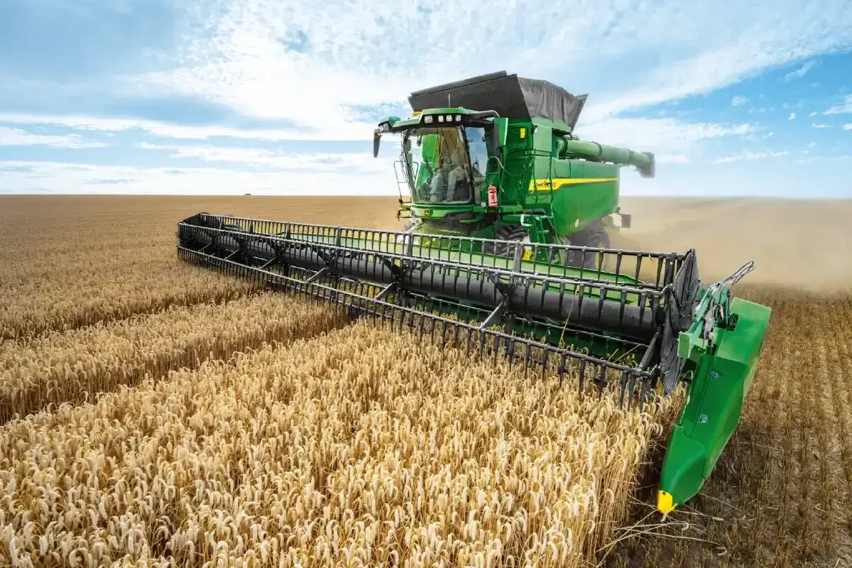 Zielony kombajn John Deere zbiera dojrzałe zboże na polu. R&oacute;żne rodzaje kombajn&oacute;w pracują wydajnie.