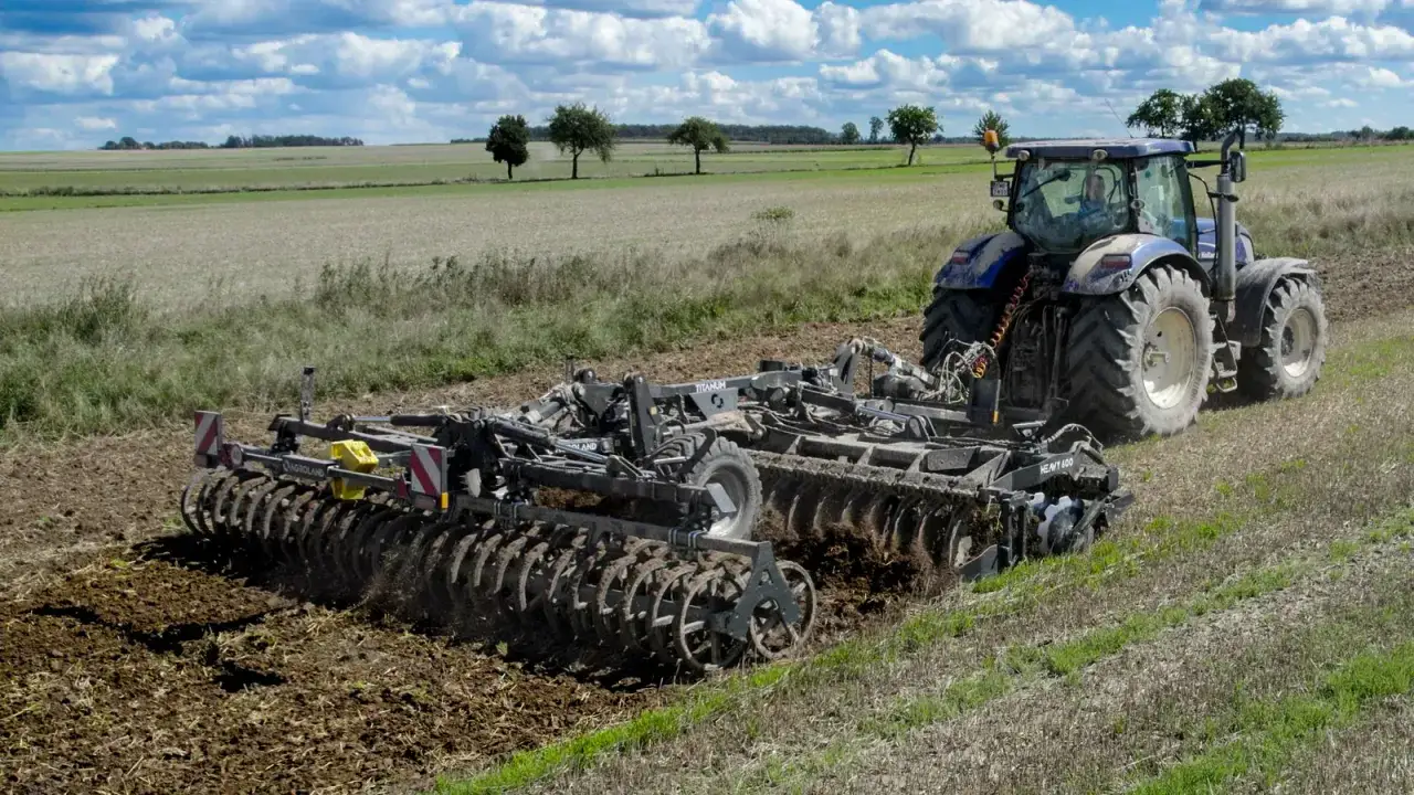 Traktor z brona łopatkową pracuje na polu, przygotowując ziemię do siewu.