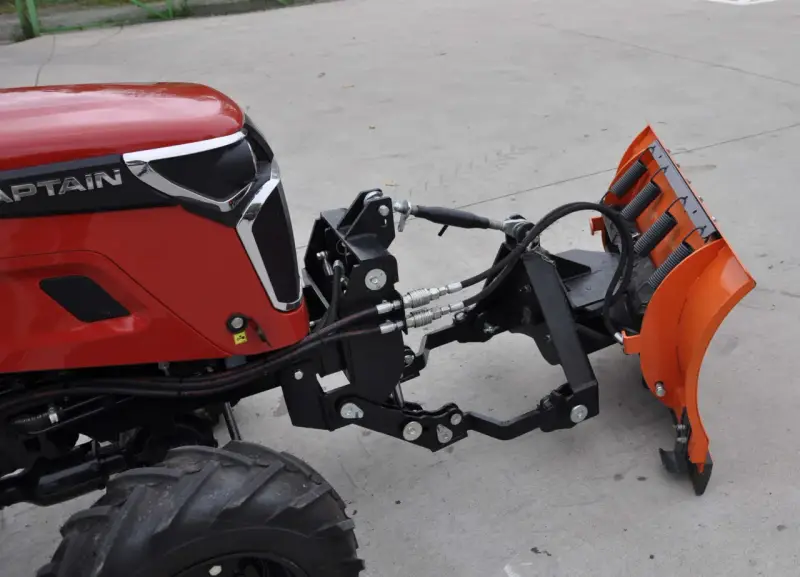 Czerwony traktor z zamontowanym z przodu pługiem śnieżnym. To jest **tuz** do pługa.