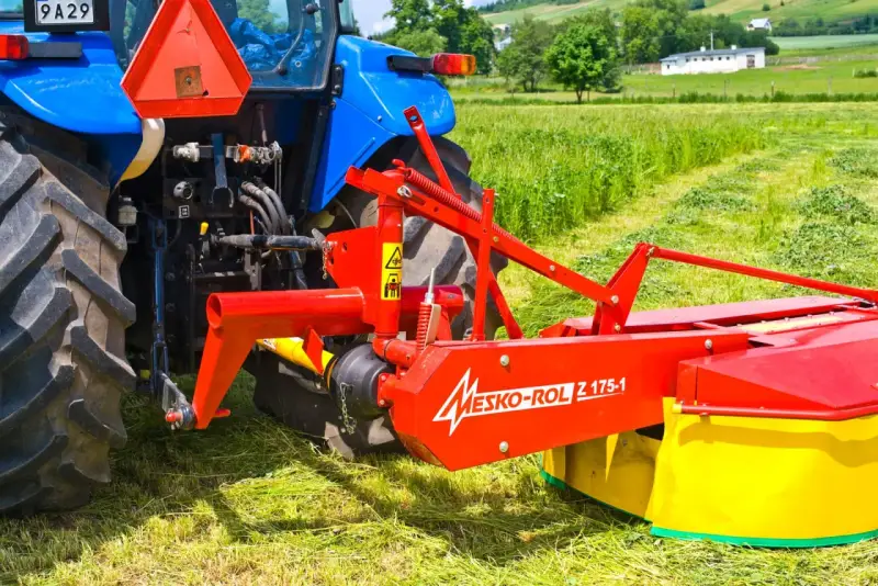 Kosiarka rotacyjna Mesko-Rol Z 175-1 zamontowana z tyłu niebieskiego traktora, gotowa do pracy na zielonej łące.
